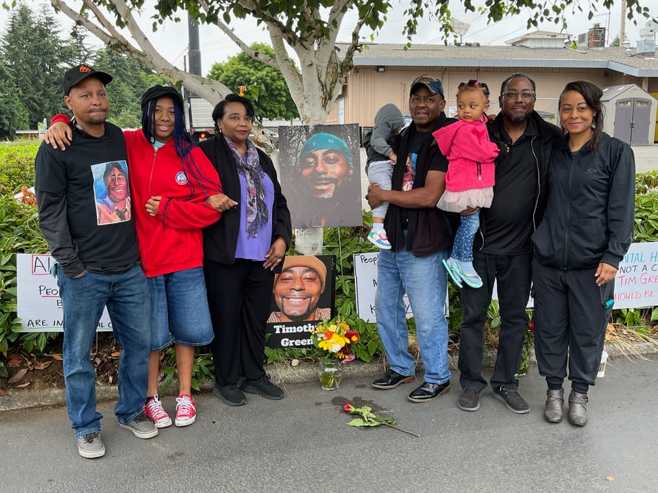 The family of Timothy Green, a 37-year-old Black man killed by police, stand in a parking lot with pictures of Green.